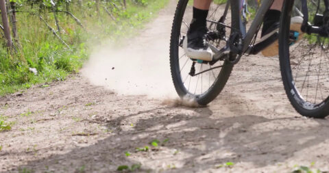 Fahrradreifen und Schuh auf Pedal wirbeln Staub auf unbefestigtem Weg; Fahrradtour in Kaltern