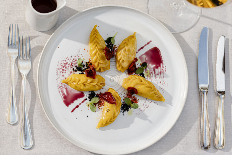 Sechs gelbe Dessert-Quenelles auf weißem Teller mit roten Saucenstrichen, Beeren und Kräuter, serviert im Hotel Haus am Hang.
