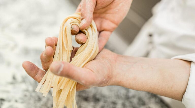Zwei Hände formen frische Bandnudeln aus Teig in einer Hotelküche