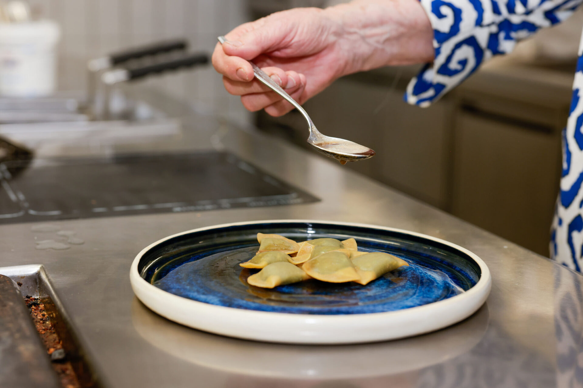 Hand mit Pinzette platziert sternförmiges gelbes Element auf blauem Teller mit dunkler Sauce in einer Hotelküche.
