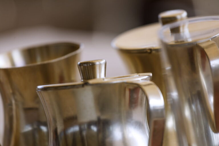 Nahaufnahme mehrerer silberner Metallkännchen auf Tablett, Vordergrund scharf, Hintergrund unscharf