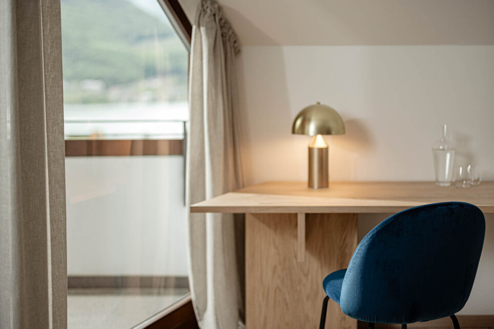 Holzablage mit goldener Pilzlampe, blauem Stuhl, hellem Vorhang und Fenster mit unscharfer Außenansicht