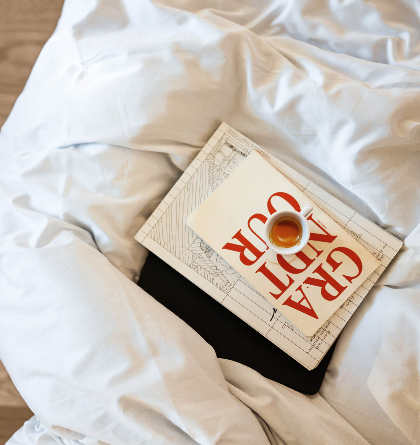 Buch mit roter Schrift auf wei&szlig;em Umschlag liegt auf zerknitterter wei&szlig;er Bettdecke, darunter schwarzes Tablett