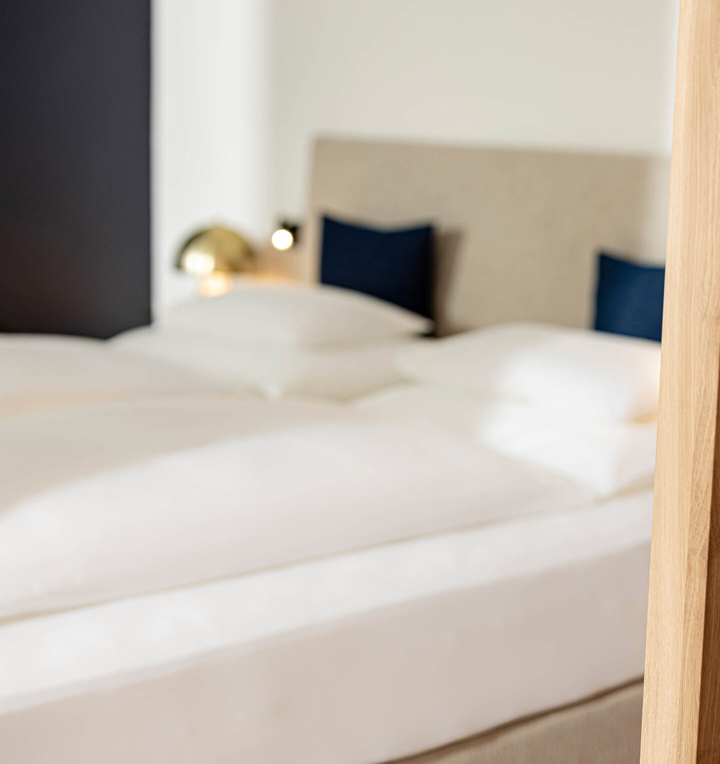 Zwei getrennte Betten mit wei&szlig;er Bettw&auml;sche, gepolstertem Kopfteil, blauen Kissen und goldener Wandlampe in See Suite 103.