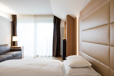 Doppelzimmer in Hotel-Suite mit Doppelbett, gepolstertem Kopfteil, Vorhang und bodentiefer Glasfront mit Balkon.