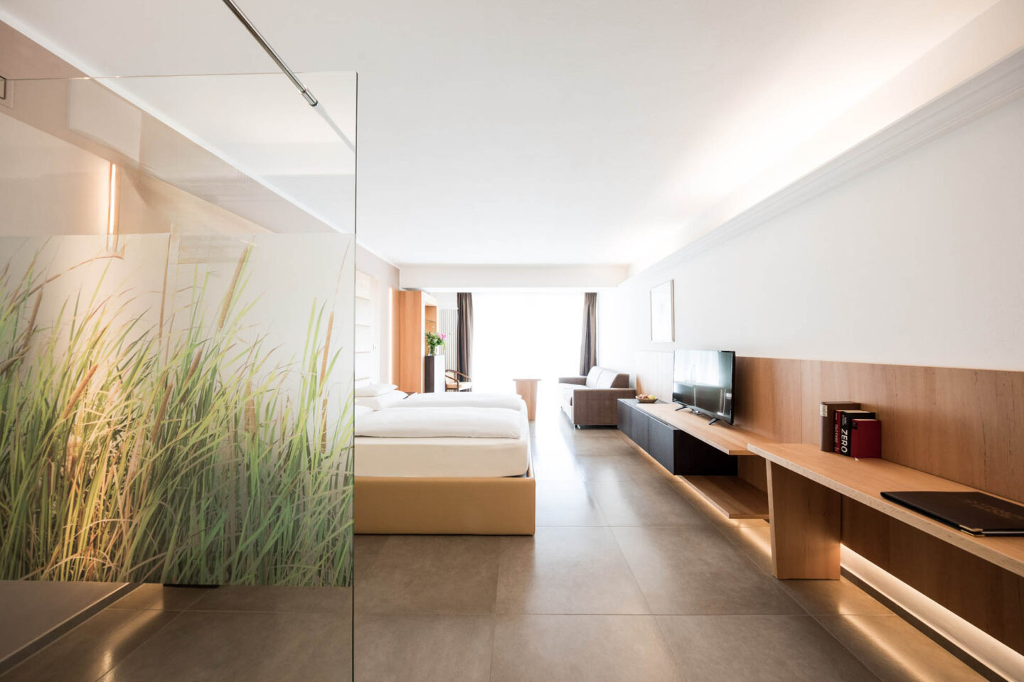 Helles Doppelzimmer (Suite Süd) mit Bett, Sitzbereich, Schreibtisch und großer Terrassentür sowie dekorativem Glasraumteiler.