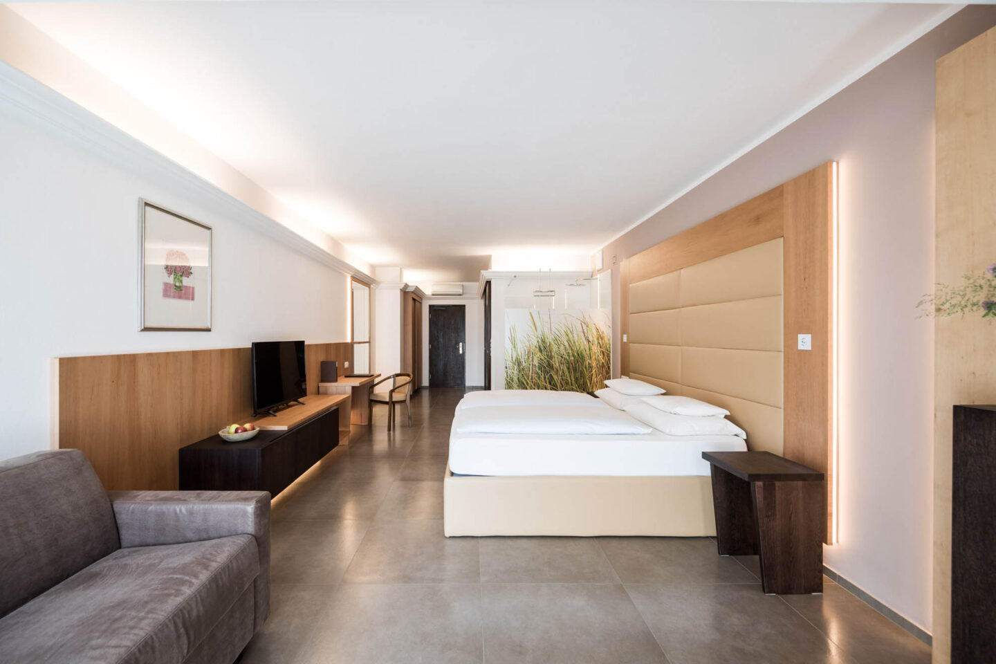 Helles Doppelzimmer der Suite Süd im Haus am Hang mit Doppelbett, Holzkopfteil, TV-Konsole, Sitzbereich und großem Fenster.