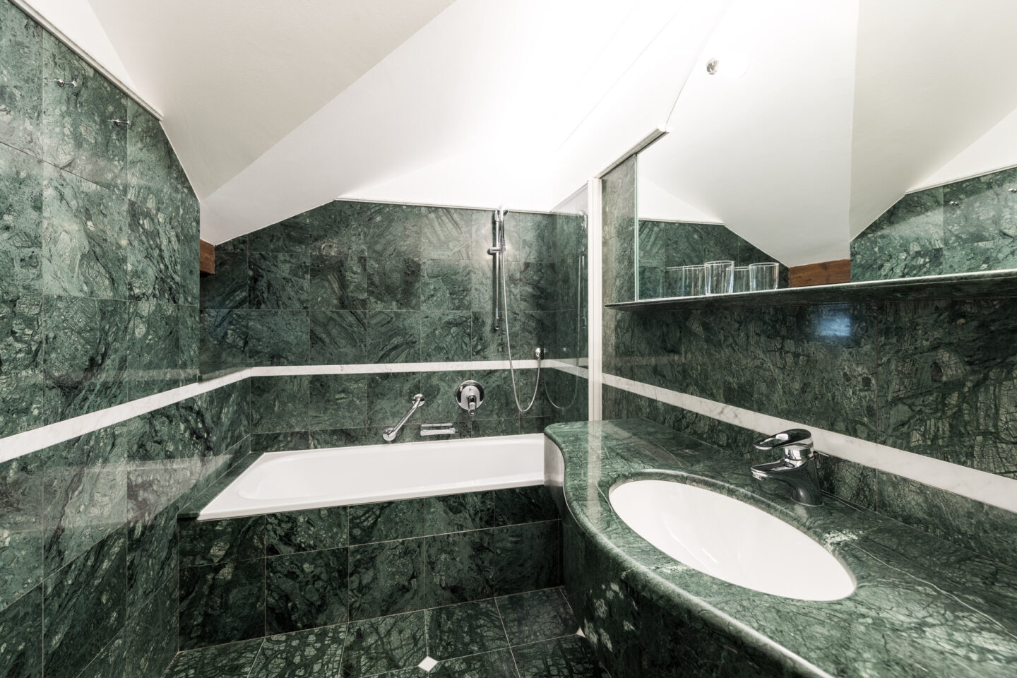 Grünes Marmorbad: Badewanne unter Dachschräge mit Dachfenster, Handbrause, Waschbecken mit ovalem Spiegel und Ablage.