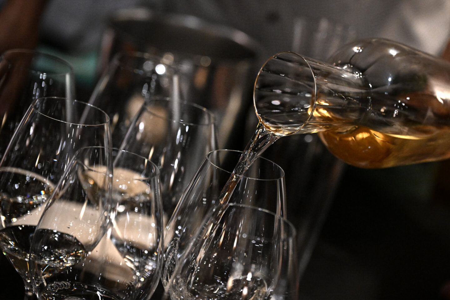 Mehrere Weingläser aufgereiht, eines wird mit goldenem Weißwein aus einer Karaffe eingeschenkt.