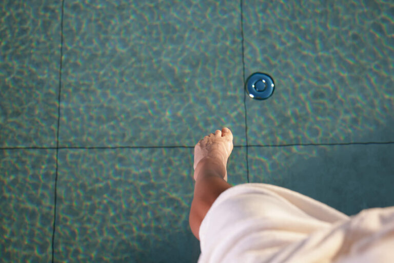 Rechter Fuß über türkis gefliestem Becken, daneben weißer Stoff und rundes Ablaufgitter