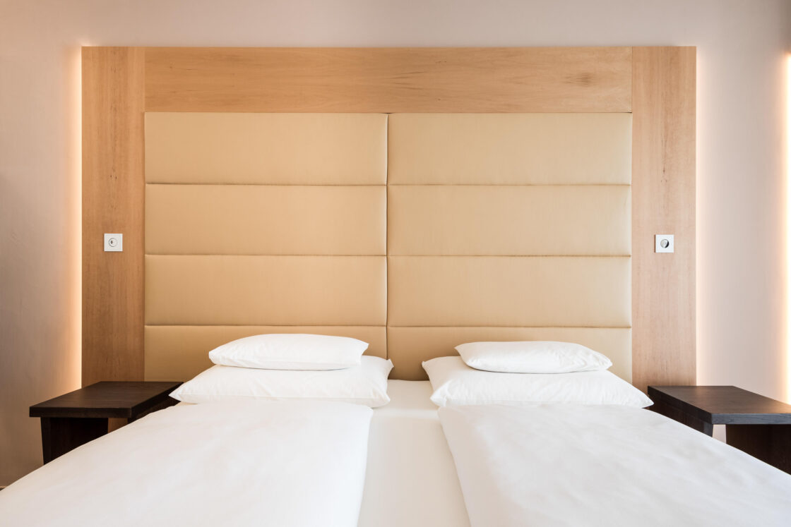 Zwei getrennte Betten mit weißer Bettwäsche in Suite, großes gepolstertes helles Kopfteil und helles Holzrahmen