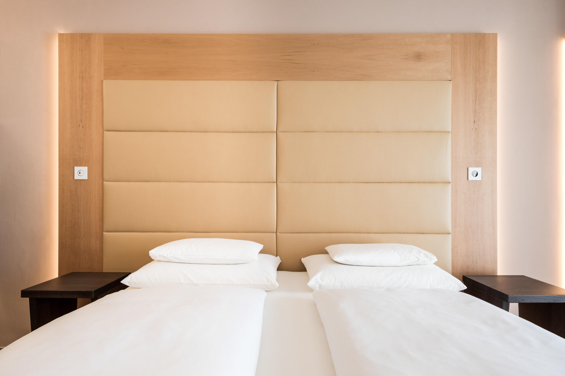 Zwei getrennte Betten mit weißer Bettwäsche in Suite, großes gepolstertes helles Kopfteil und helles Holzrahmen