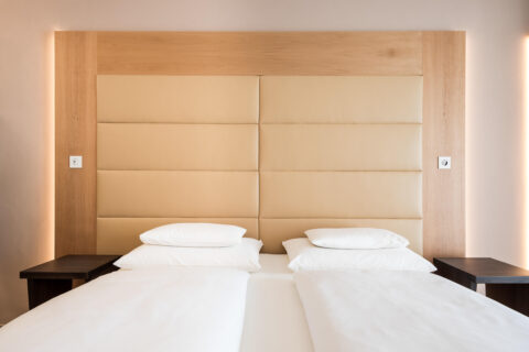 Zwei getrennte Betten mit weißer Bettwäsche in Suite, großes gepolstertes helles Kopfteil und helles Holzrahmen