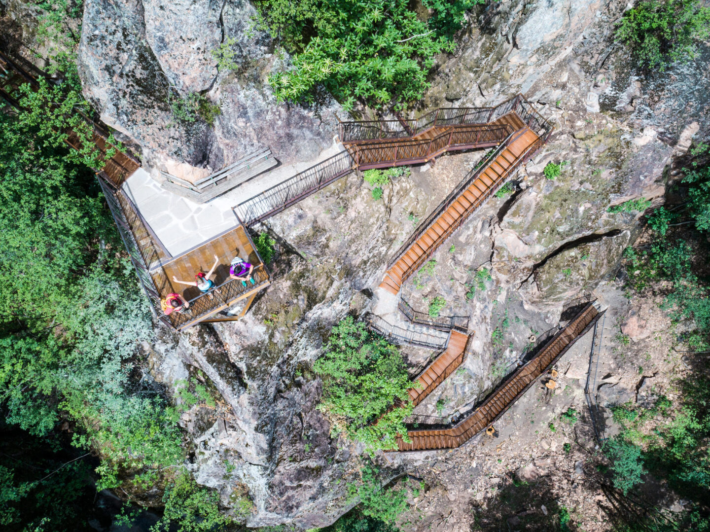 Holzstege und Treppen entlang steiler Felsflanken mit niedriger Vegetation, mehrere Aussichtsplattformen und Wanderer.
