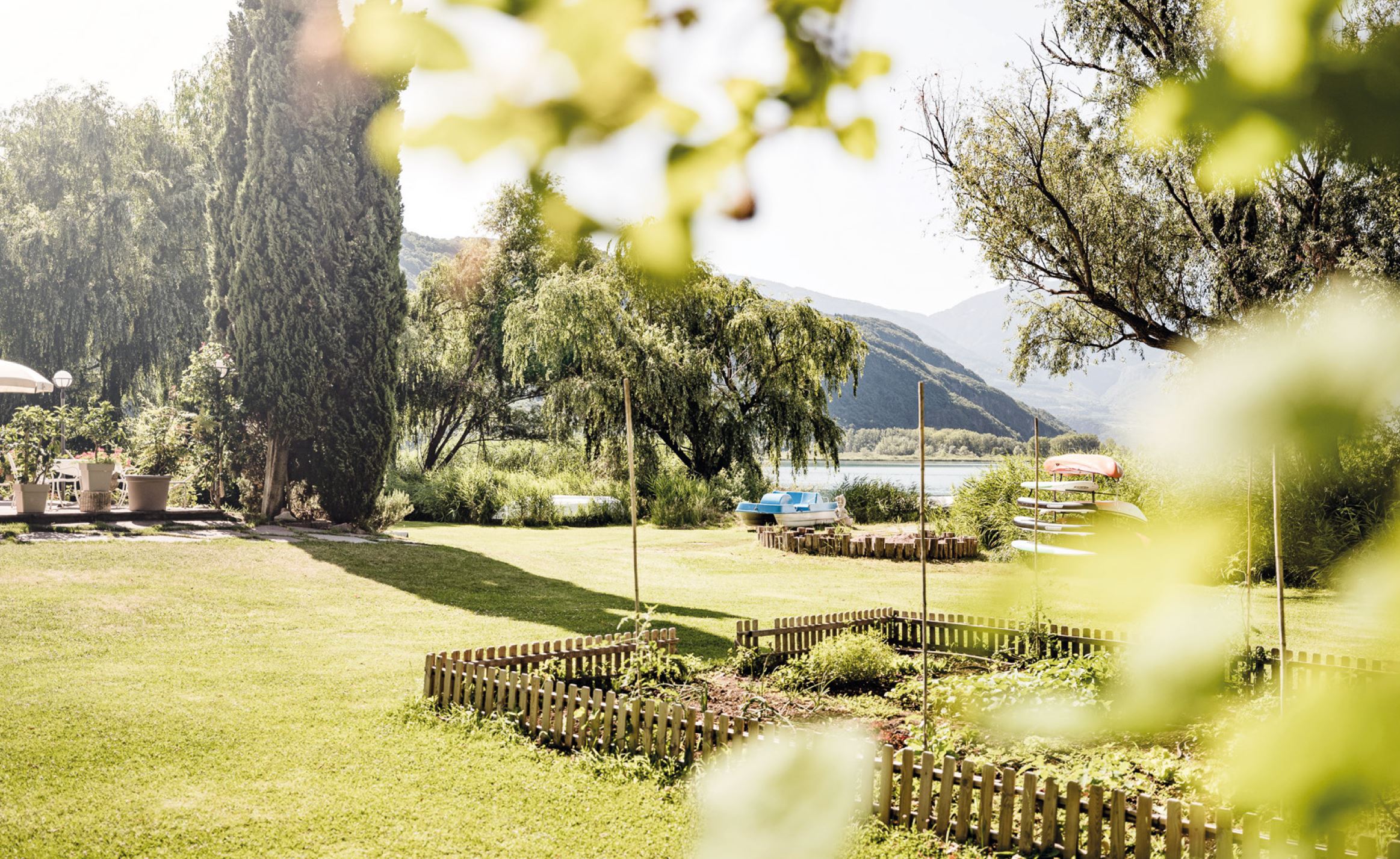 Rasen mit Blumenbeeten, Büschen und Sitzbereich, Blick auf See und Berge im Hintergrund