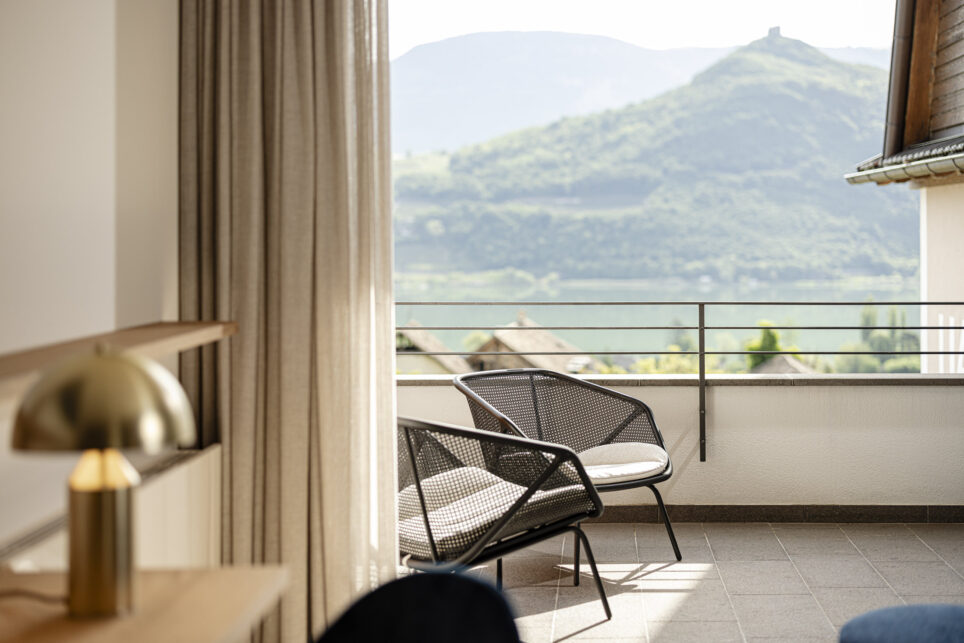 Balkon eines Tagungshotels mit zwei Stühlen und Geländer, Blick auf den Kalterer See und bewaldete Hügel