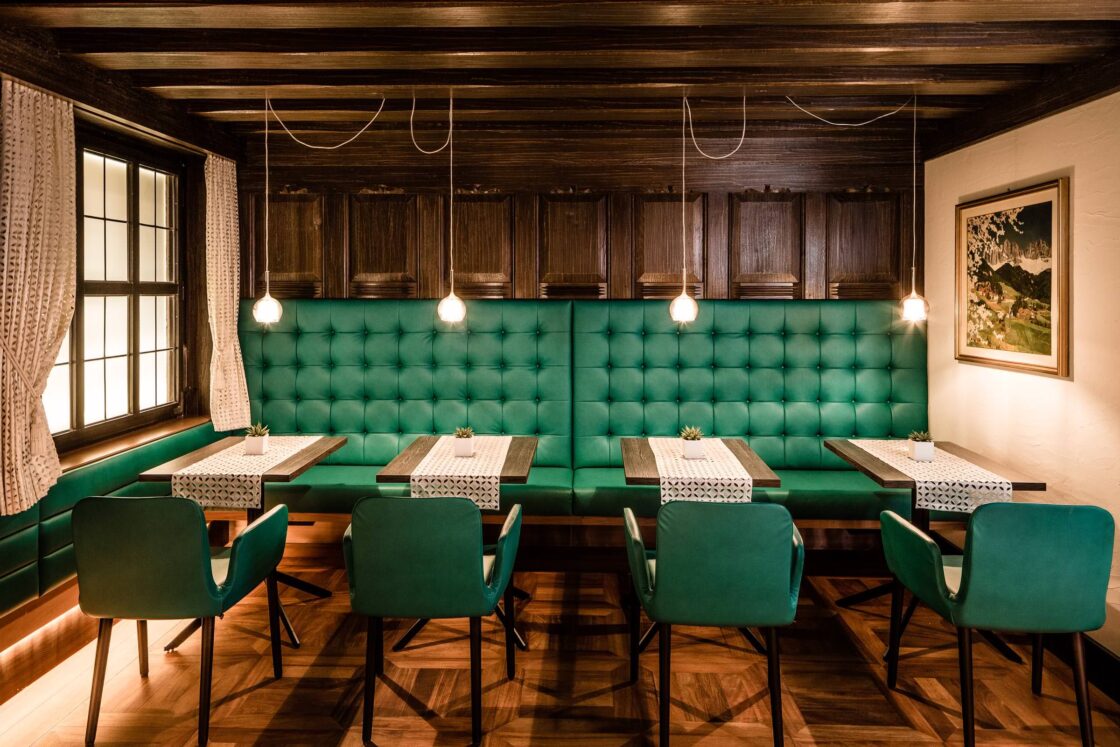 Gastraum mit grünen Polsterbänken und Stühlen, dunkler Holzverkleidung, kleinen Tischen und Parkettboden.