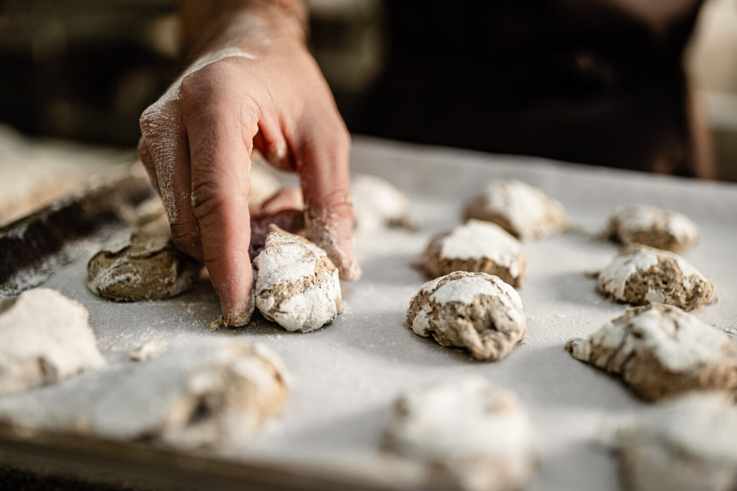 Hand formt puderzuckerbestäubte Teiglinge auf mit Backpapier belegtem Backblech