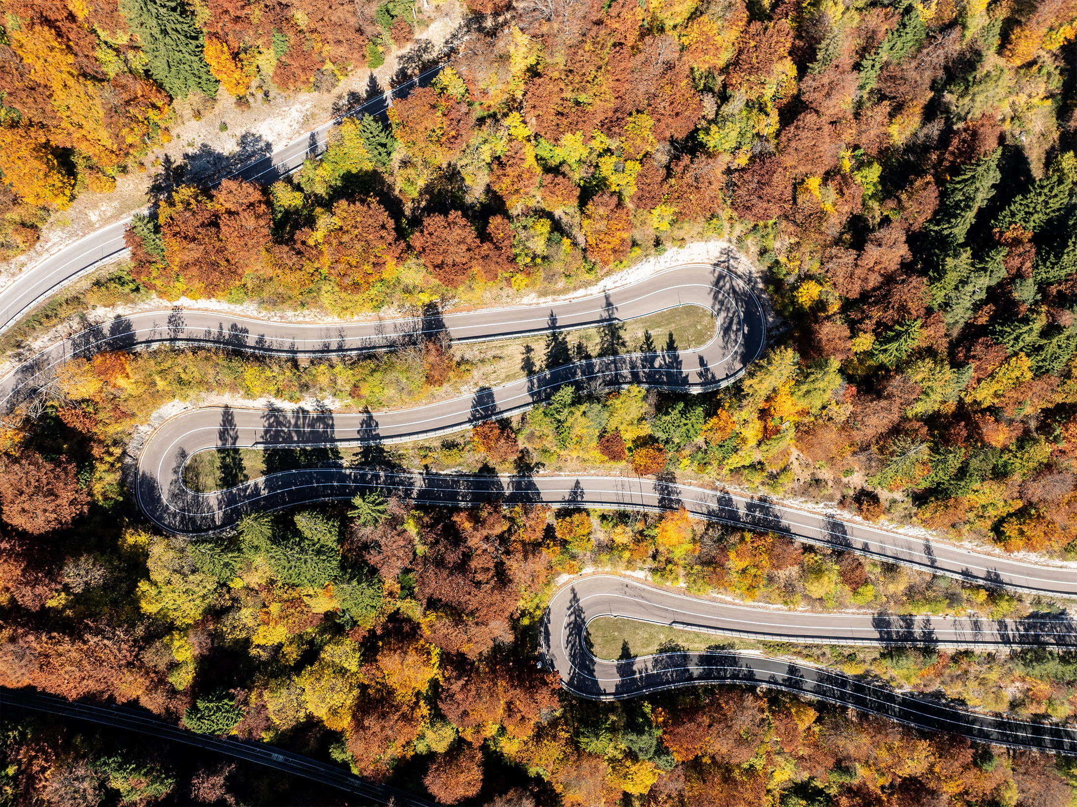 Luftaufnahme einer kurvigen Serpentinenstraße mit mehreren Kehren durch bunten Herbstwald